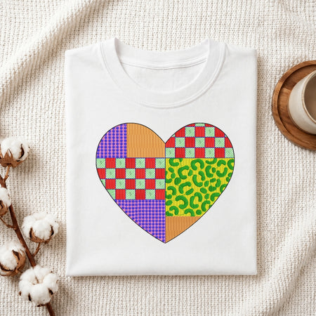 A colorful heart embroidery design featuring patchwork patterns displayed within a wooden hoop on white fabric, with thread spools nearby.