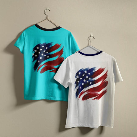 Two t-shirts hanging on hangers, one turquoise and one white, both printed with a stylized brushstroke American flag graphic.