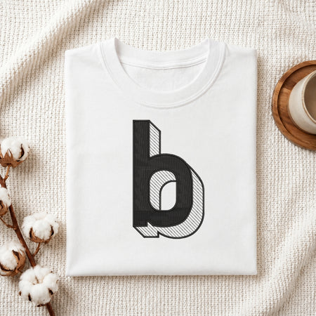 A neatly folded white crewneck t-shirt featuring a stitched 3D block lowercase letter "b" design, styled with cotton branches and a wooden coaster.