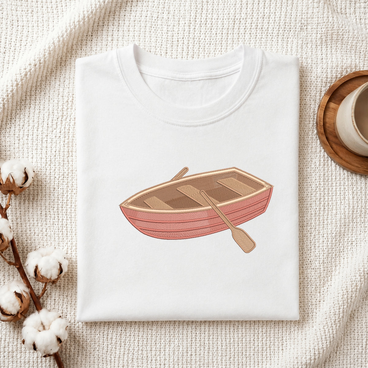 Wooden rowboat with oars embroidery design stitched on a folded white t-shirt mockup.