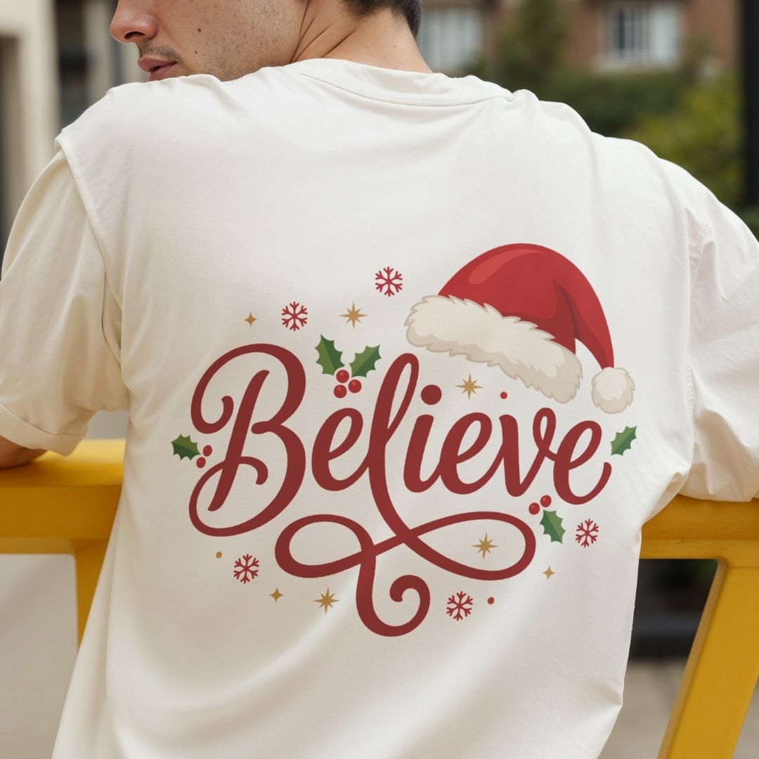 Person wearing a cream-colored t-shirt with a "Believe" holiday graphic printed on the back.