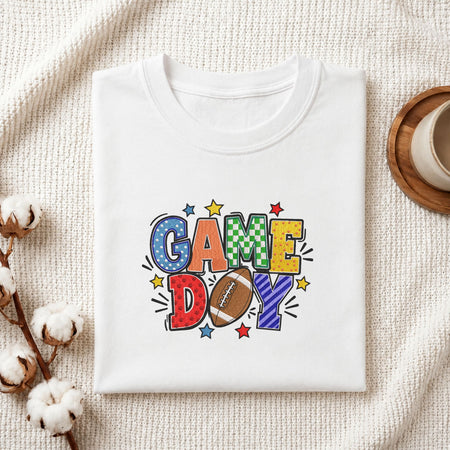 Folded white cotton t-shirt mockup featuring a "Game Day" football machine embroidery design, styled with cotton stems and a wooden cup   