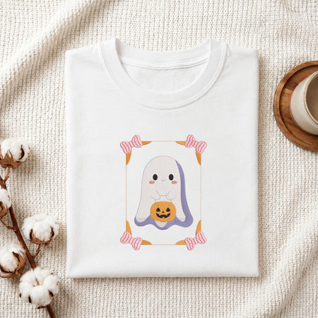 Folded white cotton t-shirt mockup featuring a cute ghost machine embroidery design, styled with cotton stems and a wooden cu