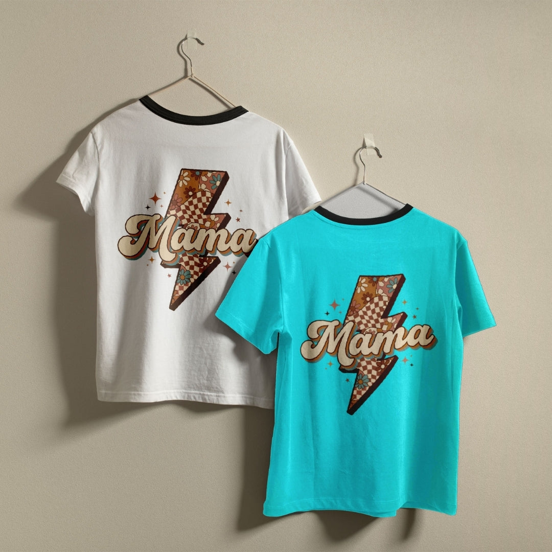 Two ringer t-shirts with black neckbands hanging on metal hangers against a beige wall. One shirt is white and the other is turquoise, both featuring a retro-style graphic with a lightning bolt, checkered pattern, and the word 'Mama' in cursive.