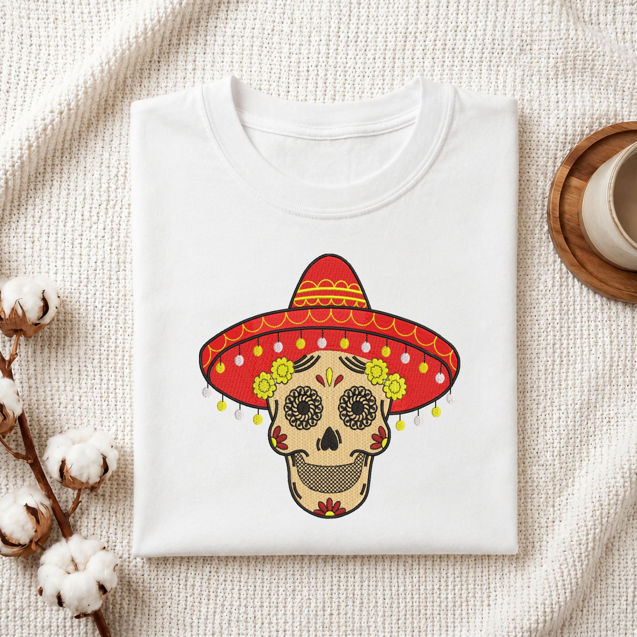 Folded white t-shirt featuring a sugar skull with a red sombrero embroidery design.