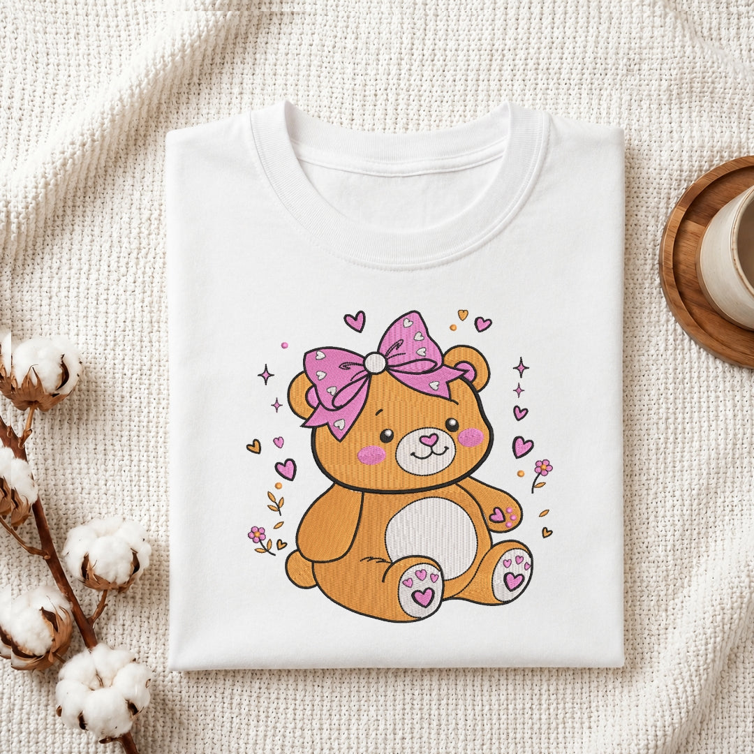 Adorable teddy bear embroidery stitched onto a folded white t-shirt.