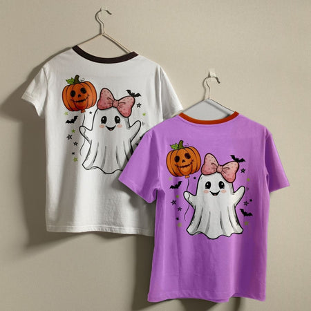 Two children's ringer t-shirts with a Halloween ghost and pumpkin graphic, shown on hangers against a beige wall. One shirt is white with a dark brown collar, and the other is purple with an orange collar.