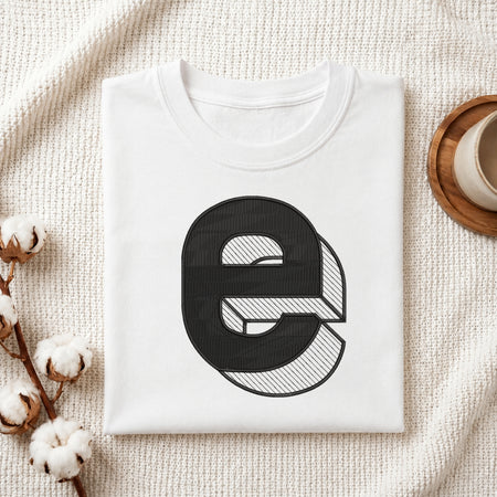 A neatly folded white crewneck t-shirt featuring a stitched 3D block lowercase letter "e" design, styled with cotton branches and a wooden coaster.