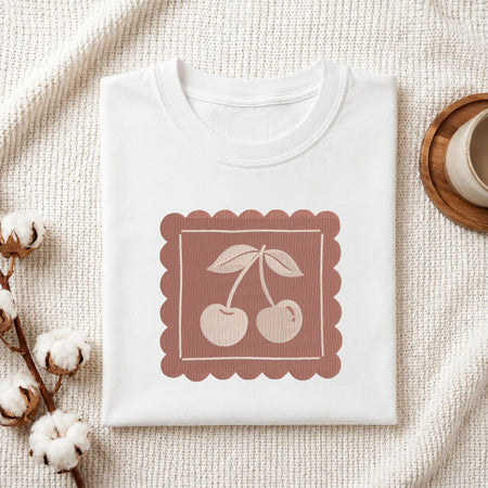 Folded white cotton t-shirt mockup featuring a vintage cherry machine embroidery design, styled with cotton stems and a wooden cup