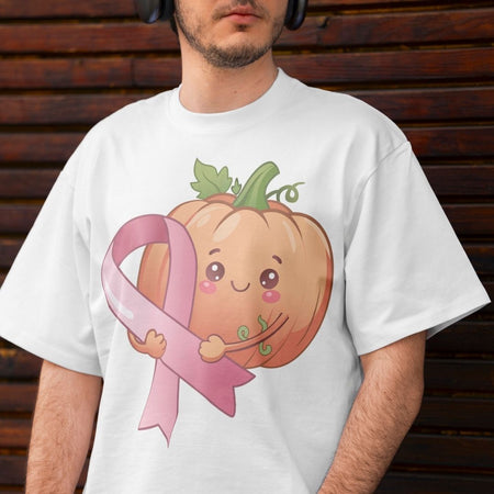 A man wearing a white t-shirt with a cute graphic of a smiling orange pumpkin hugging a pink ribbon, set against a dark brown wooden background.