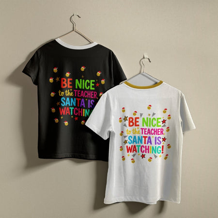 Two kids' short-sleeve t-shirts hanging on hangers against a plain beige wall. The left shirt is black with a colorful text graphic on the back reading 'BE NICE to the TEACHER, SANTA IS WATCHING!' and small candy illustrations.