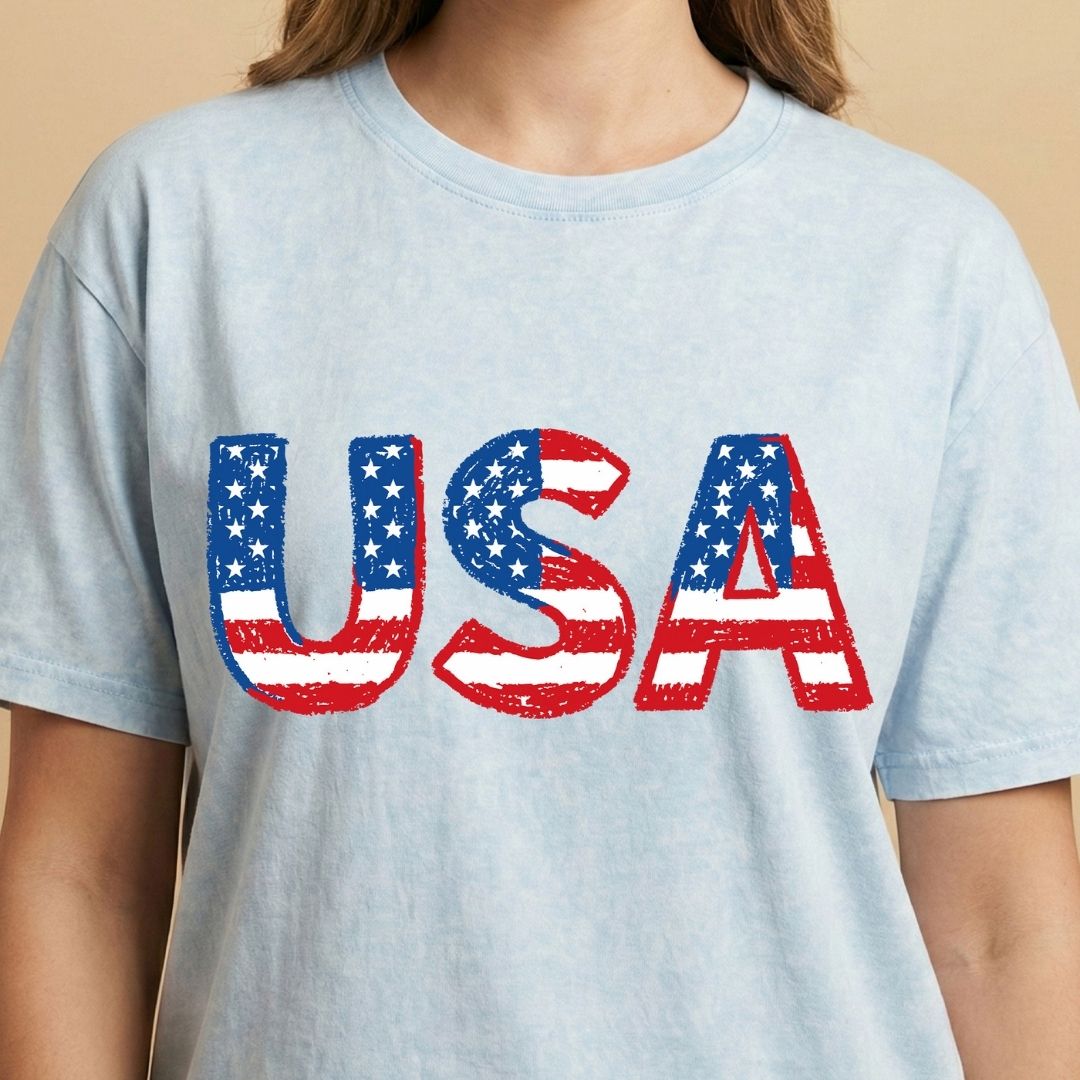 Light blue t-shirt with 'USA' printed in American flag colors on a beige background