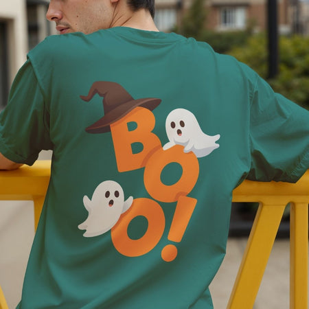 Back view of a person wearing a dark green t-shirt featuring a large Halloween "BOO!" graphic with playful ghosts and a witch hat.