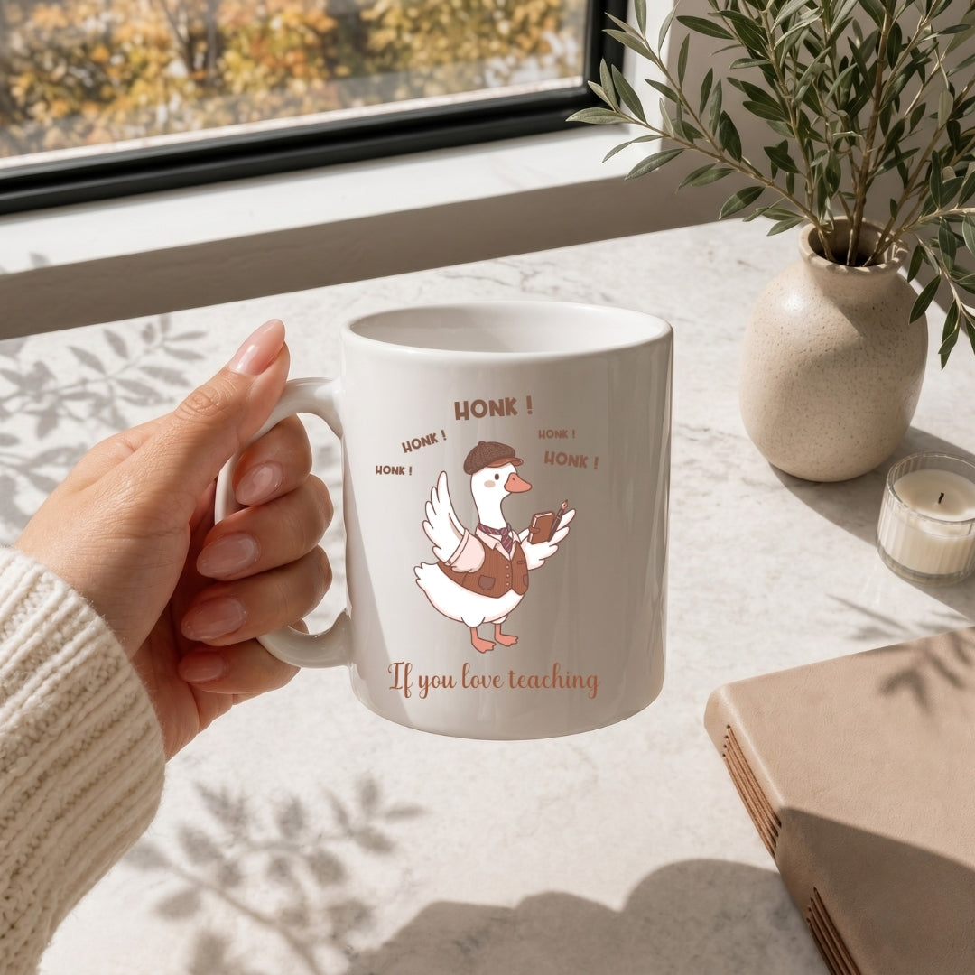 Hand holding a white ceramic coffee mug printed with the funny "HONK! If you love teaching" duck illustration.