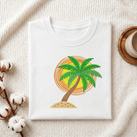 A folded white t-shirt with a colorful palm tree graphic, styled on a textured cream fabric with cotton bolls and a wooden cup in the background.