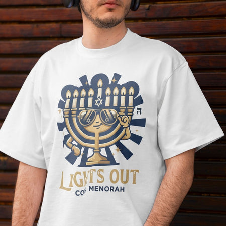 Two t-shirts hanging side-by-side—one white and one bright neon green—both printed with a cool cartoon Hanukkah menorah graphic and the words "LIGHTS OUT COOL MENORAH".