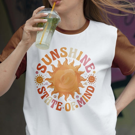 Person wearing a white t-shirt with a sun graphic and 'Sunshine State of Mind' text, drinking from a glass.