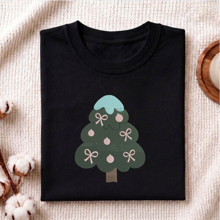 Folded black cotton t-shirt mockup featuring a Christmas tree machine embroidery design, styled with cotton stems and a wooden cup.