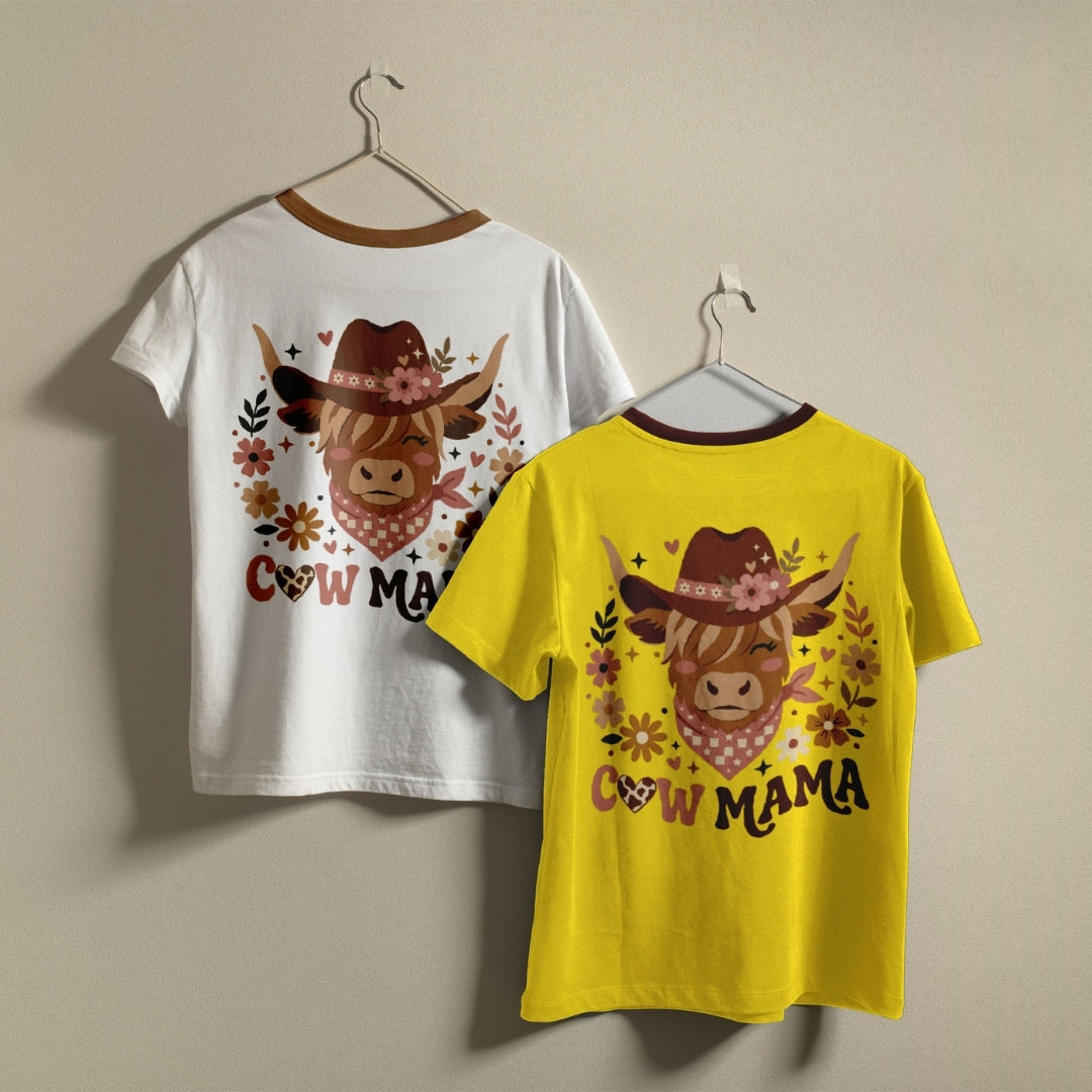 Two short-sleeve ringer T-shirts hanging on hangers against a plain beige wall. The left shirt is white with a brown collar and features a cowgirl cow graphic with the text 'COW MAMA' in brown.