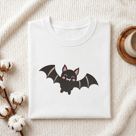 Folded white cotton t-shirt mockup featuring a cute Halloween bat machine embroidery design, styled with cotton stems and a wooden cup.