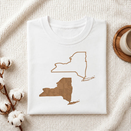  Folded white cotton t-shirt mockup featuring New York state map machine embroidery designs, styled with cotton stems and a wooden cup.   