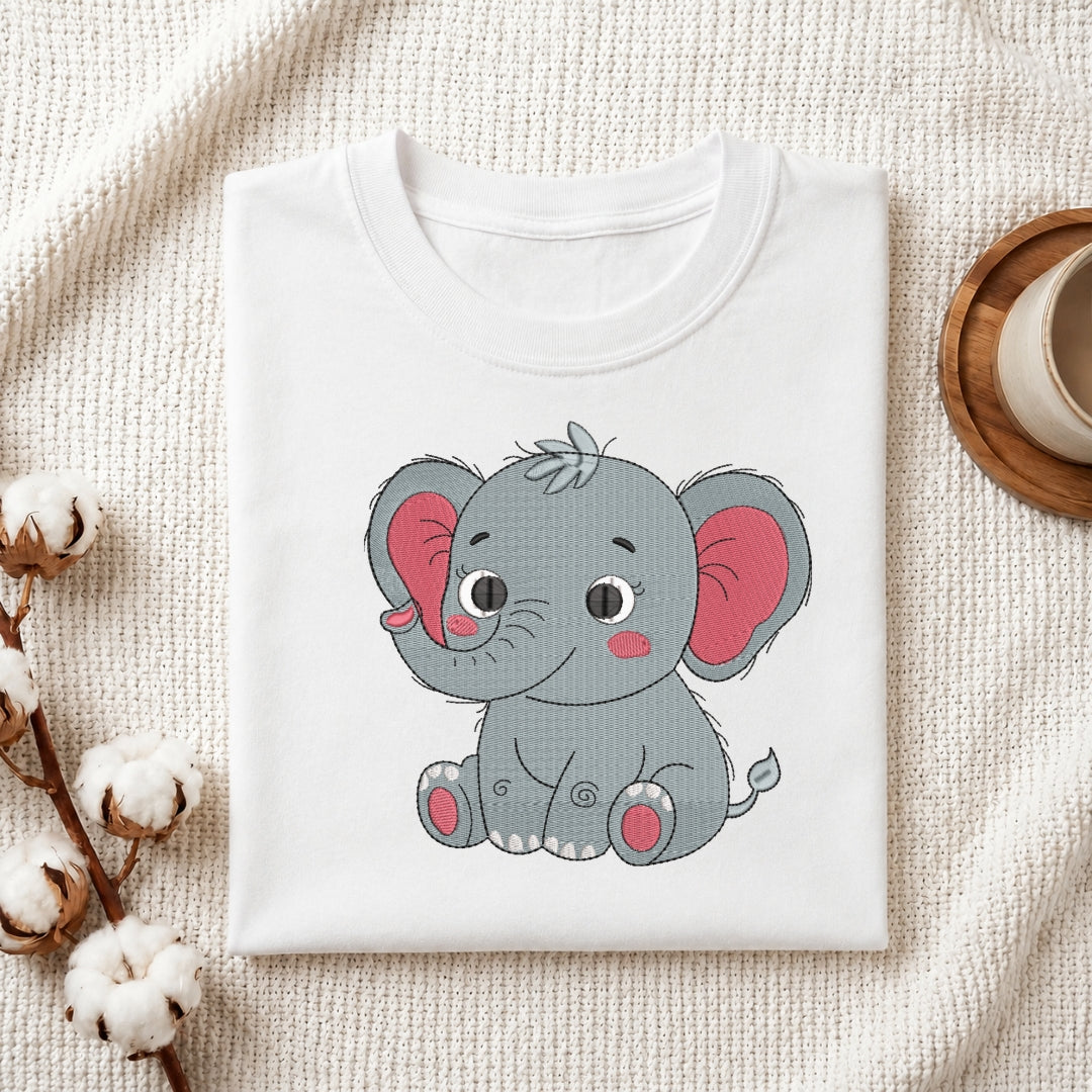 A folded white crewneck t-shirt featuring a cute cartoon baby elephant graphic, styled on a textured cream fabric background with cotton bolls and a wooden cup.