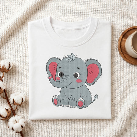 A folded white crewneck t-shirt featuring a cute cartoon baby elephant graphic, styled on a textured cream fabric background with cotton bolls and a wooden cup.