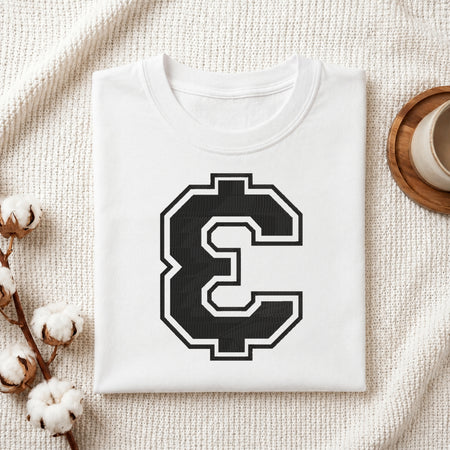 A folded white crewneck t-shirt with a large black and white block letter 'C' graphic on the front, styled on a textured cream knit blanket with cotton bolls and a wooden cup in the background.