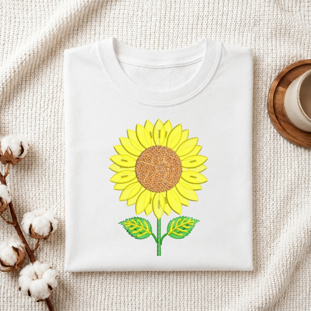 A folded white t-shirt featuring the embroidered sunflower design centered on the fabric.