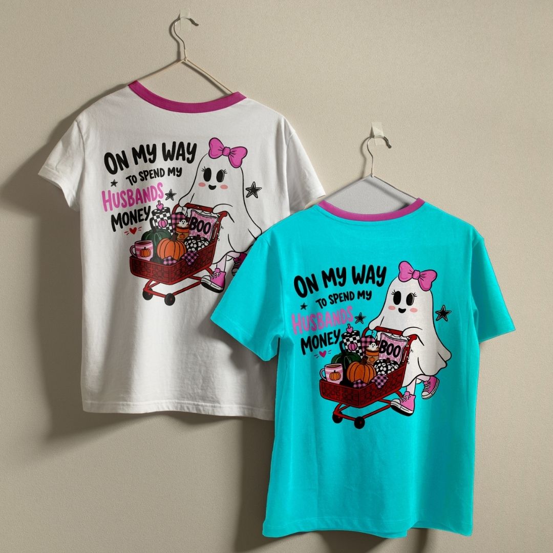 Two t-shirts in white and turquoise hanging on hangers, both displaying the ghost pushing a shopping cart Halloween design on the back.