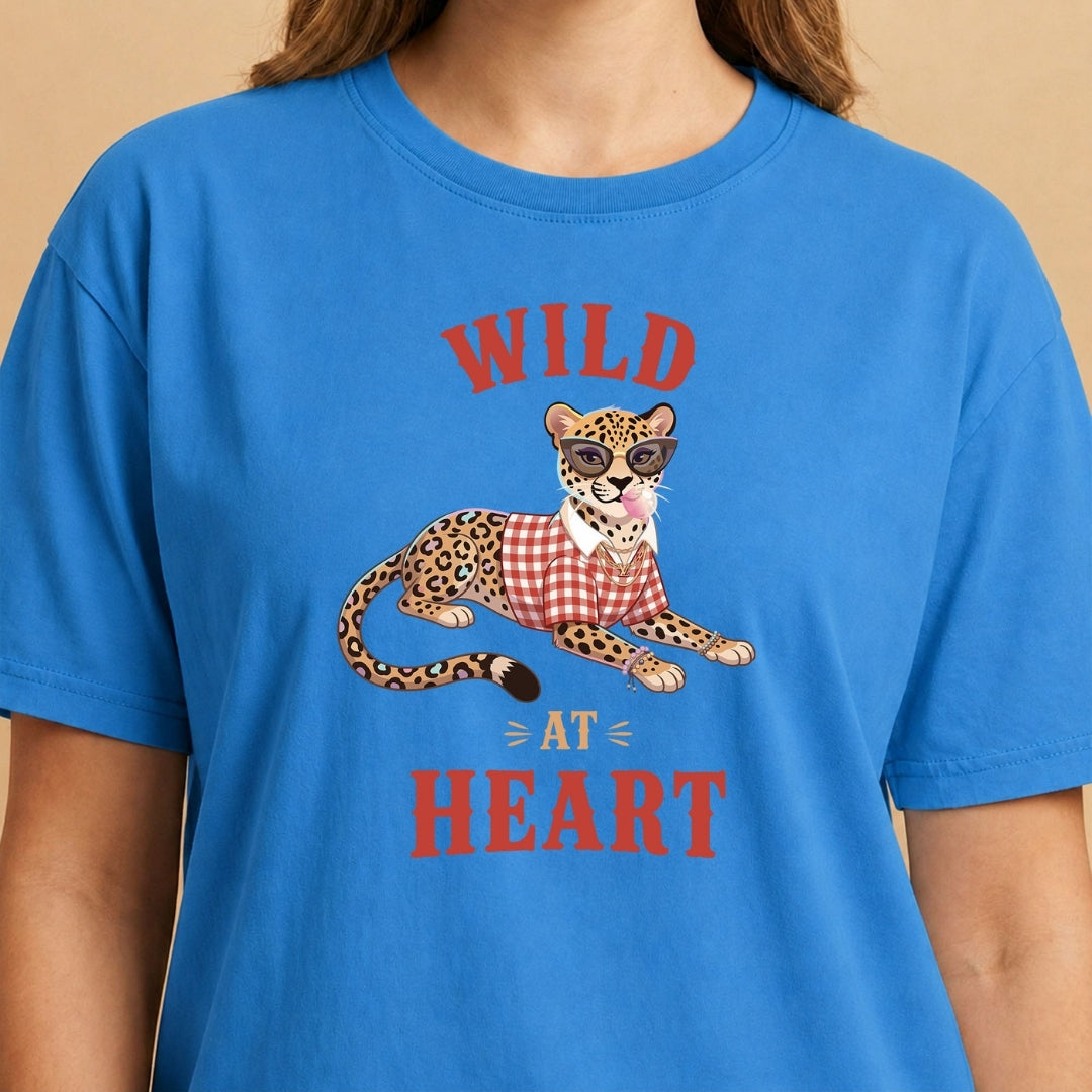 Smiling person wearing a white t-shirt featuring a trendy leopard wearing sunglasses, a gold chain, and a plaid shirt, blowing a pink bubblegum bubble, with the text "WILD AT HEART".