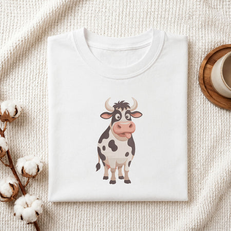 Folded white cotton t-shirt mockup featuring a funny cow machine embroidery design, styled with cotton stems and a wooden cup
