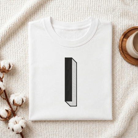 A folded white crewneck t-shirt with a minimalist black graphic of the number '1' styled on a textured cream fabric background with cotton bolls and a wooden cup.
