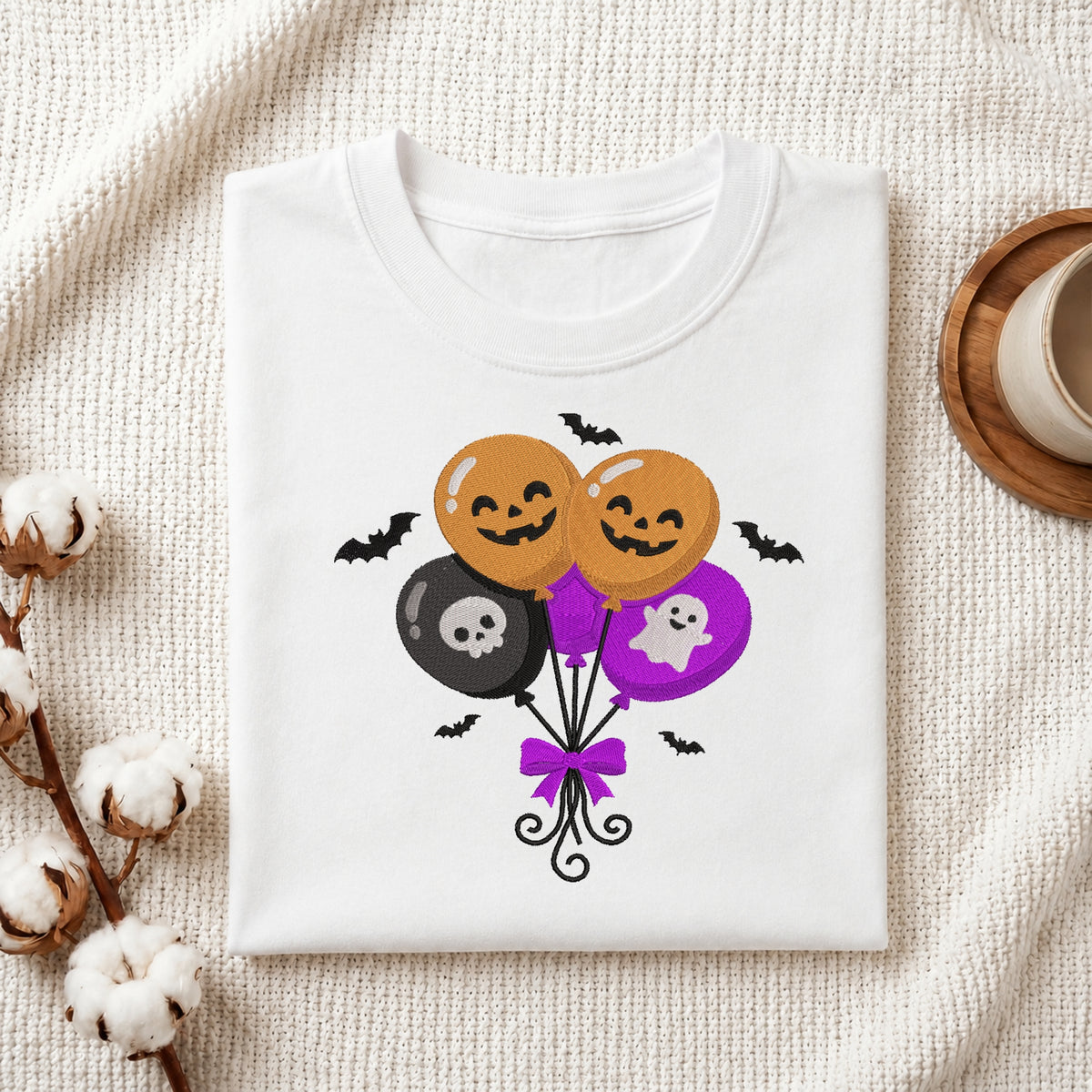 Mockup of a white folded t-shirt featuring a cute Halloween spooky balloons embroidery machine design next to cotton branches.