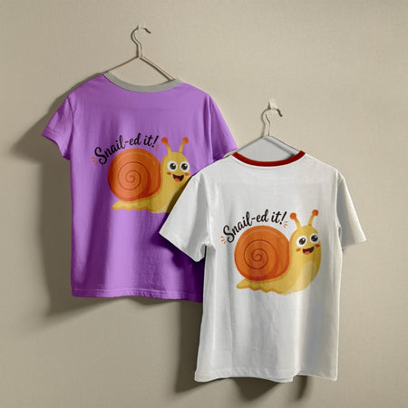 Two t-shirts hanging on hangers, one purple and one white, both printed with a smiling cartoon snail graphic and the text "Snail-ed it!".