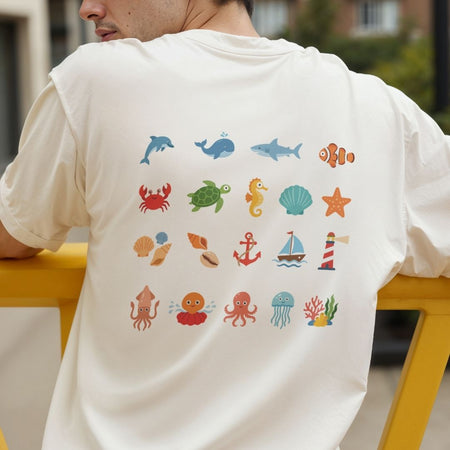 A man wearing a cream-colored t-shirt from the back, featuring a colorful grid print of various sea creatures and nautical icons including a dolphin, turtle, shark, clownfish, crab, seahorse, shell, starfish, anchor, and lighthouse.