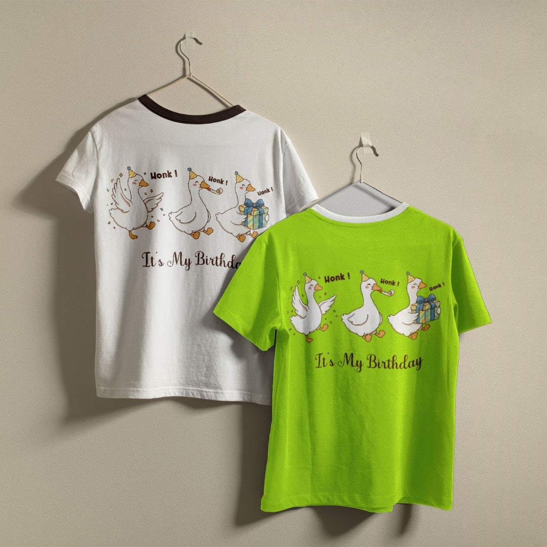 White and lime green t-shirts hanging on a wall, both displaying the humorous "It's My Birthday" partying geese graphic printed on the back.