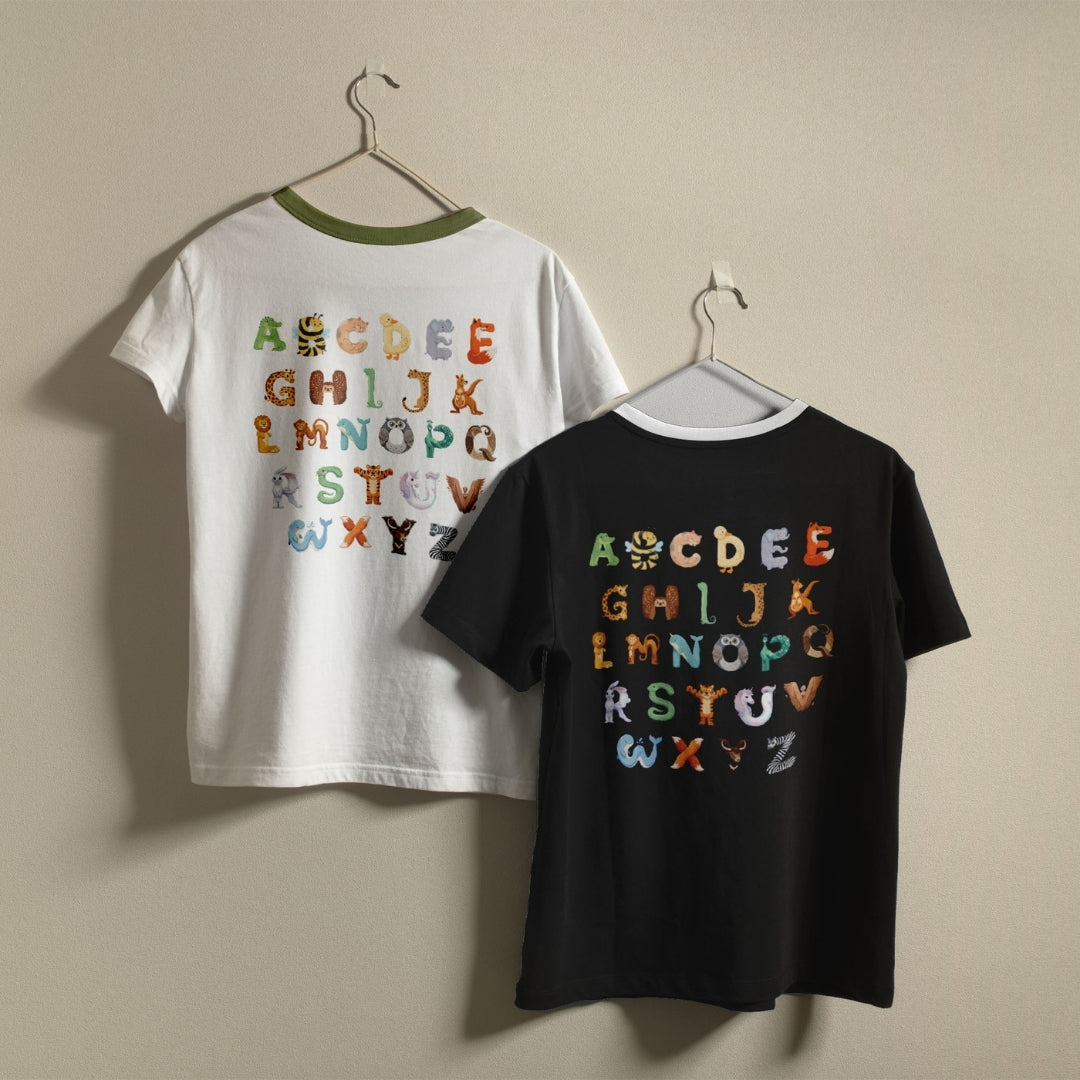 White and black t-shirts hanging on a wall, both displaying the colorful animal alphabet design printed on the back.