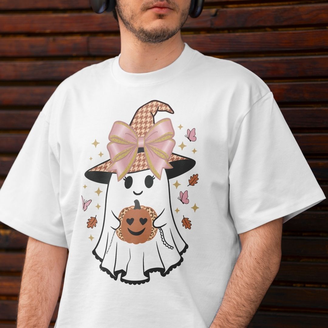 A man wearing a white graphic t-shirt with a cute cartoon ghost in a witch hat holding a pumpkin, set against a dark wooden background.