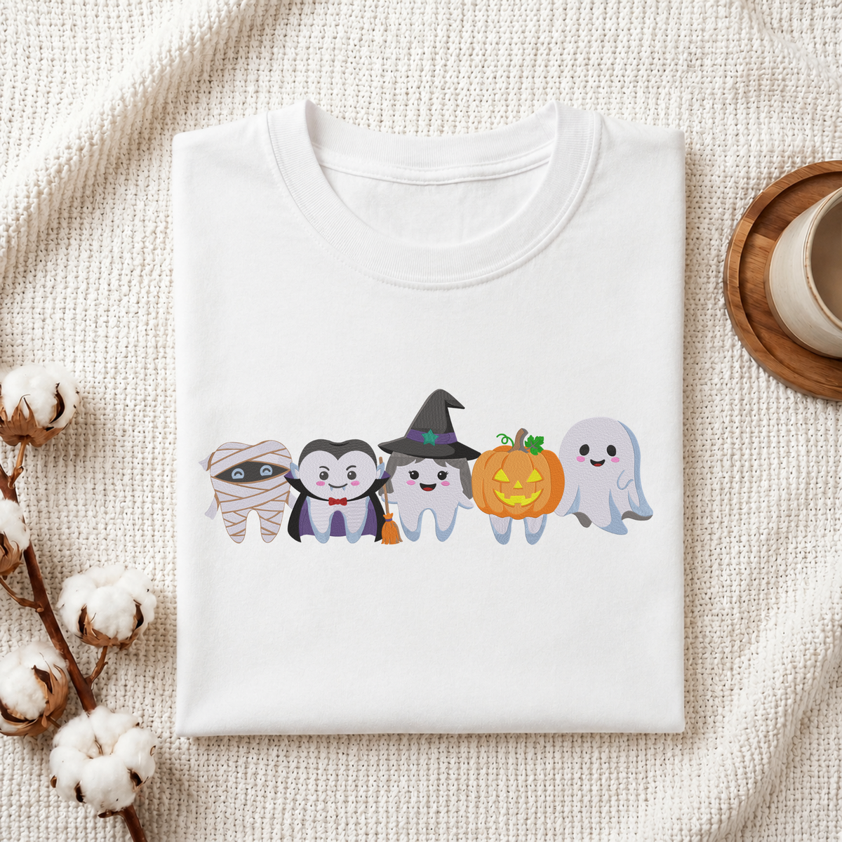 Folded white cotton t-shirt mockup featuring a cute Halloween dental teeth characters machine embroidery design, styled with cotton stems and a wooden cup