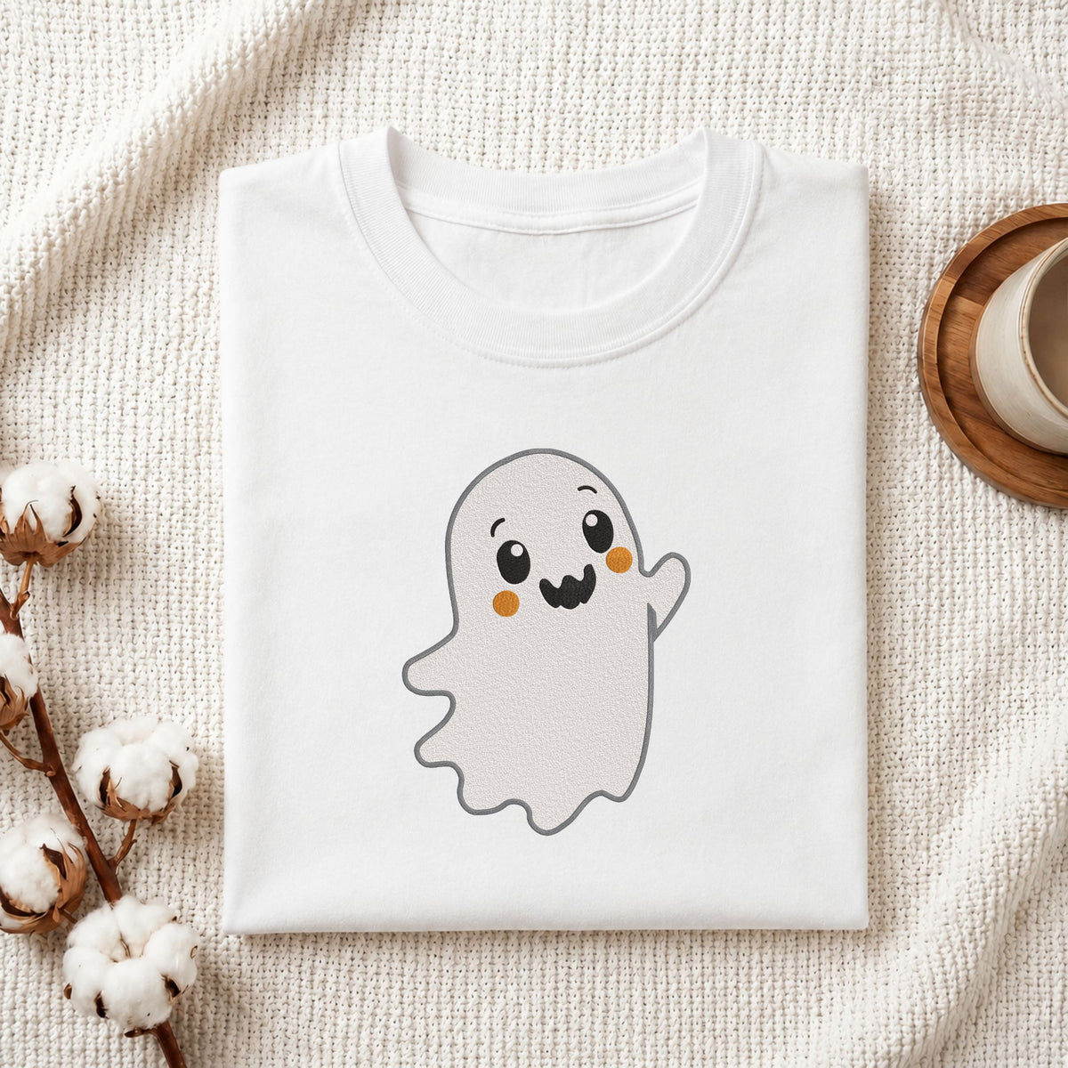  Folded white cotton t-shirt mockup featuring a cute waving ghost machine embroidery design, styled with cotton stems and a wooden cup   