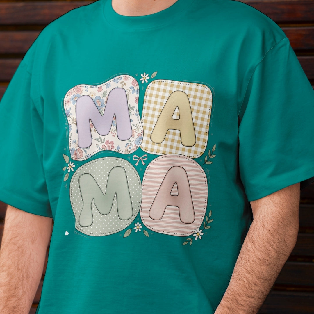 Person wearing a teal t-shirt featuring a cute pastel "MAMA" graphic with bubbly letters set inside quilted, patchwork-style shapes patterned with florals, gingham, polka dots, and stripes.