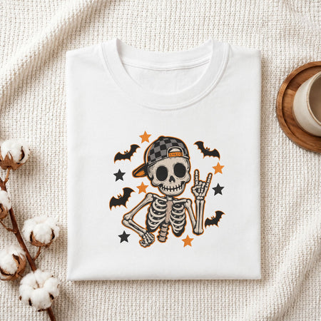Folded white cotton t-shirt mockup featuring a cute skeleton machine embroidery design, styled with cotton stems and a wooden cup
