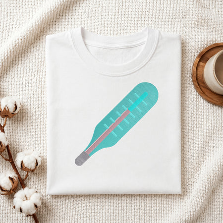A neatly folded white crewneck t-shirt featuring a stitched medical thermometer design, styled with cotton branches and a wooden coaster.