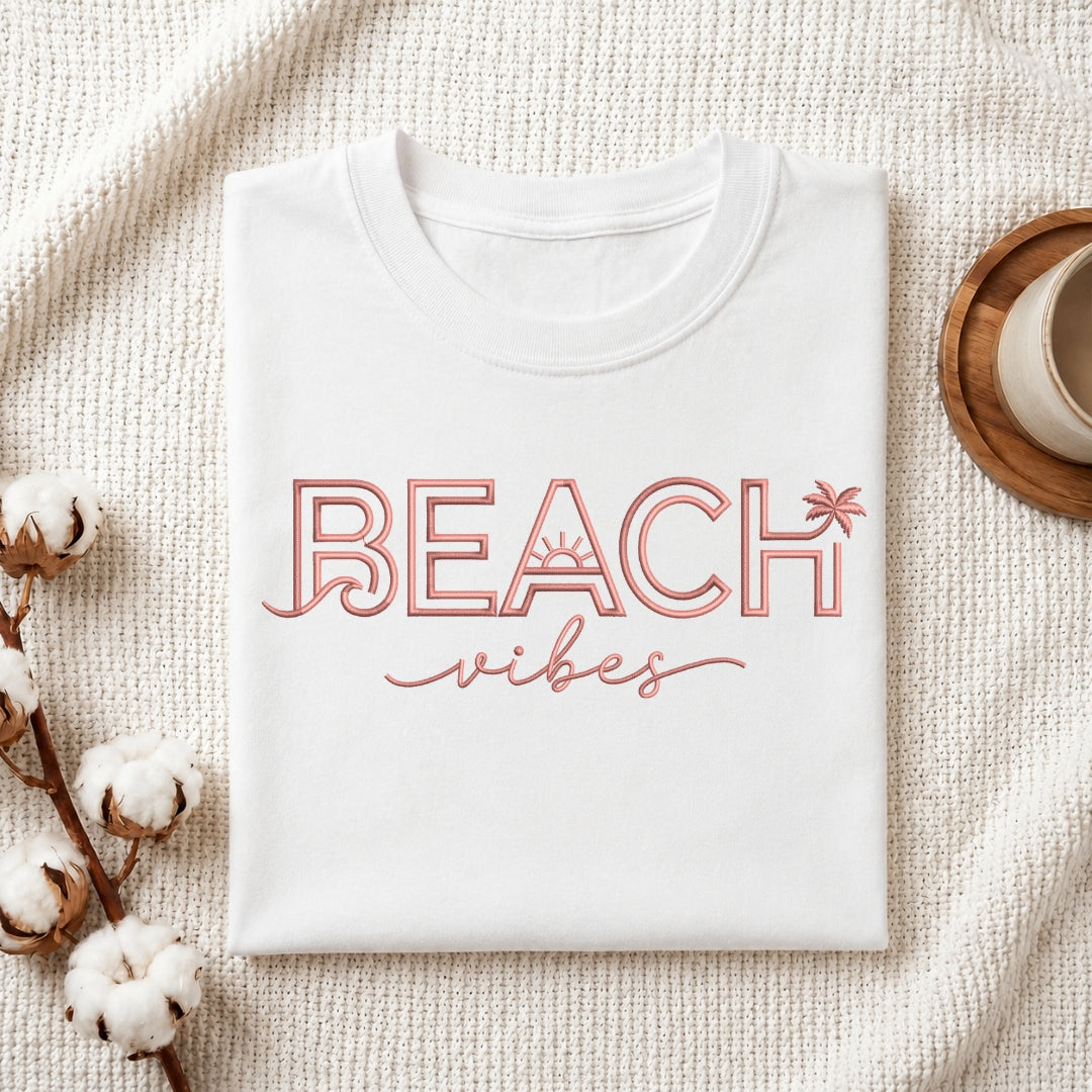 The "Beach Vibes" machine embroidery design stitched onto a white t-shirt, displayed on a textured white fabric background with cotton sprigs.