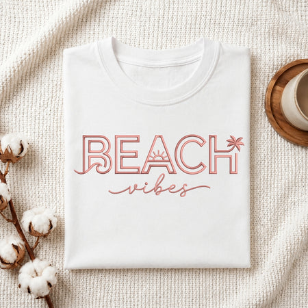 The "Beach Vibes" machine embroidery design stitched onto a white t-shirt, displayed on a textured white fabric background with cotton sprigs.