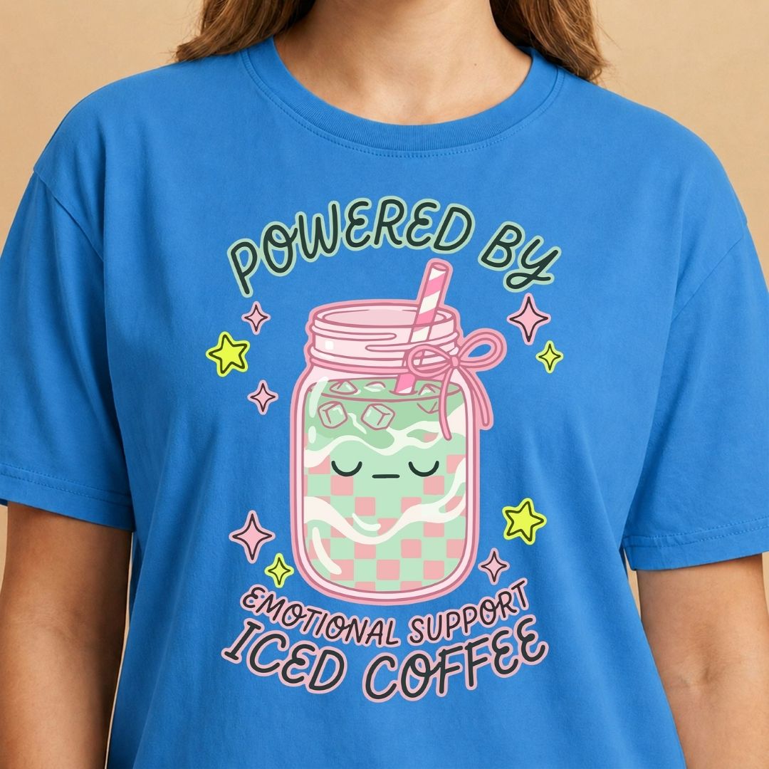 Blue t-shirt with a design of a mason jar with ice coffee and text 'Powered by Emotional Support Iced Coffee' on a beige background.