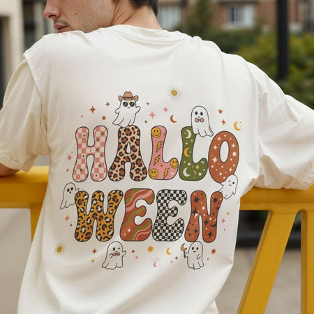 A man wearing a cream-colored t-shirt from the back, featuring a colorful 'HALLOWEEN' graphic with patterned letters and cute ghost illustrations, set against an outdoor background.