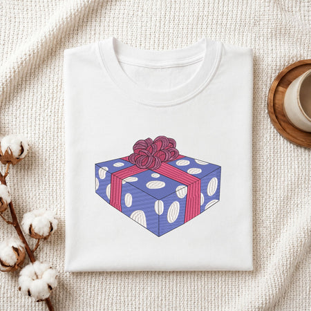 Folded white cotton t-shirt mockup featuring a wrapped gift box machine embroidery design, styled with cotton stems and a wooden cup   