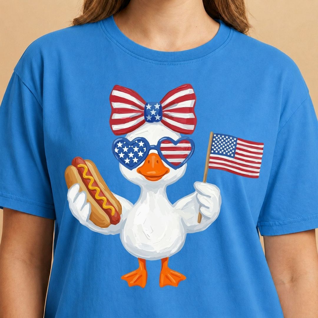 Blue t-shirt with a cartoon duck holding an American flag and a hot dog, wearing sunglasses and a bow tie.